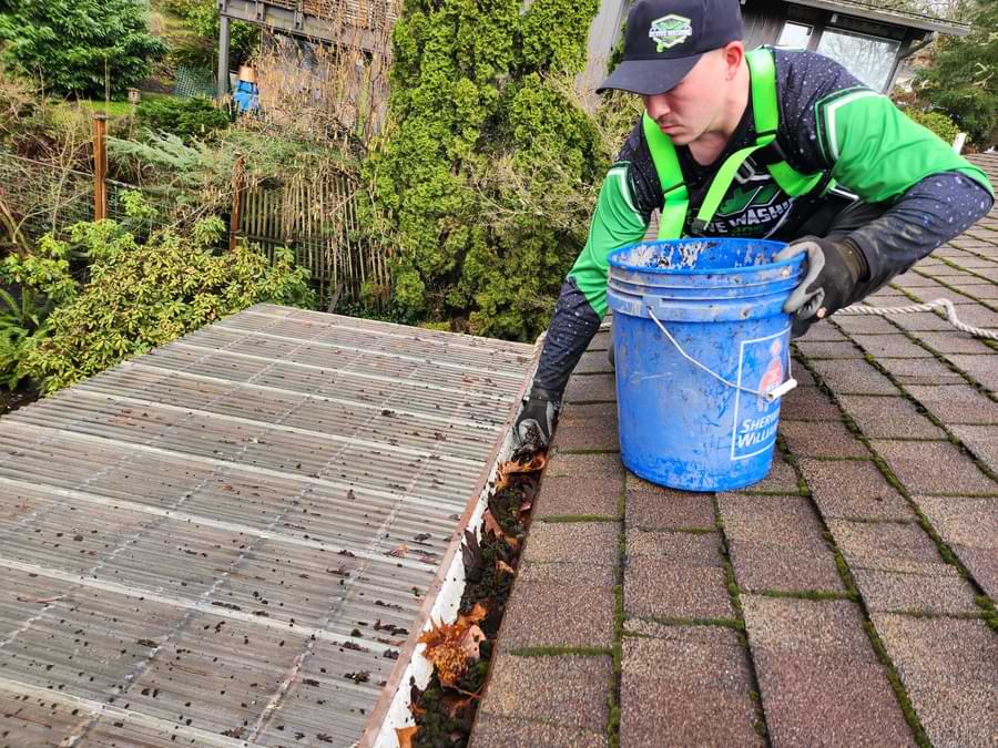 Man in safety gear on a roof cleaning leaves